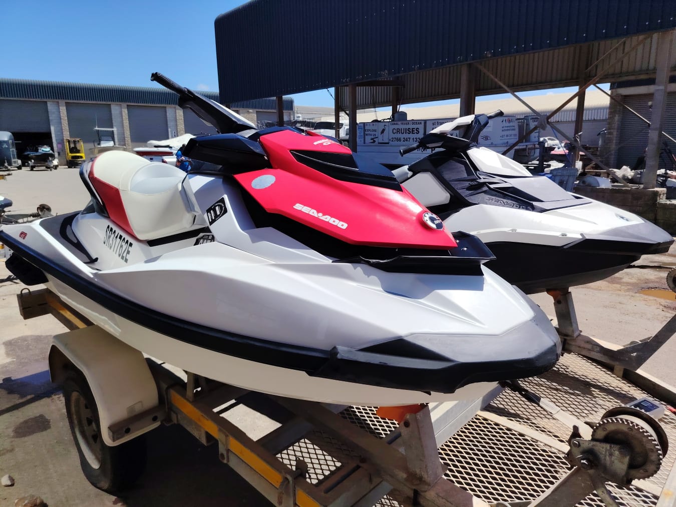 Two jet skis on a trailer with a building and clear sky in the background.