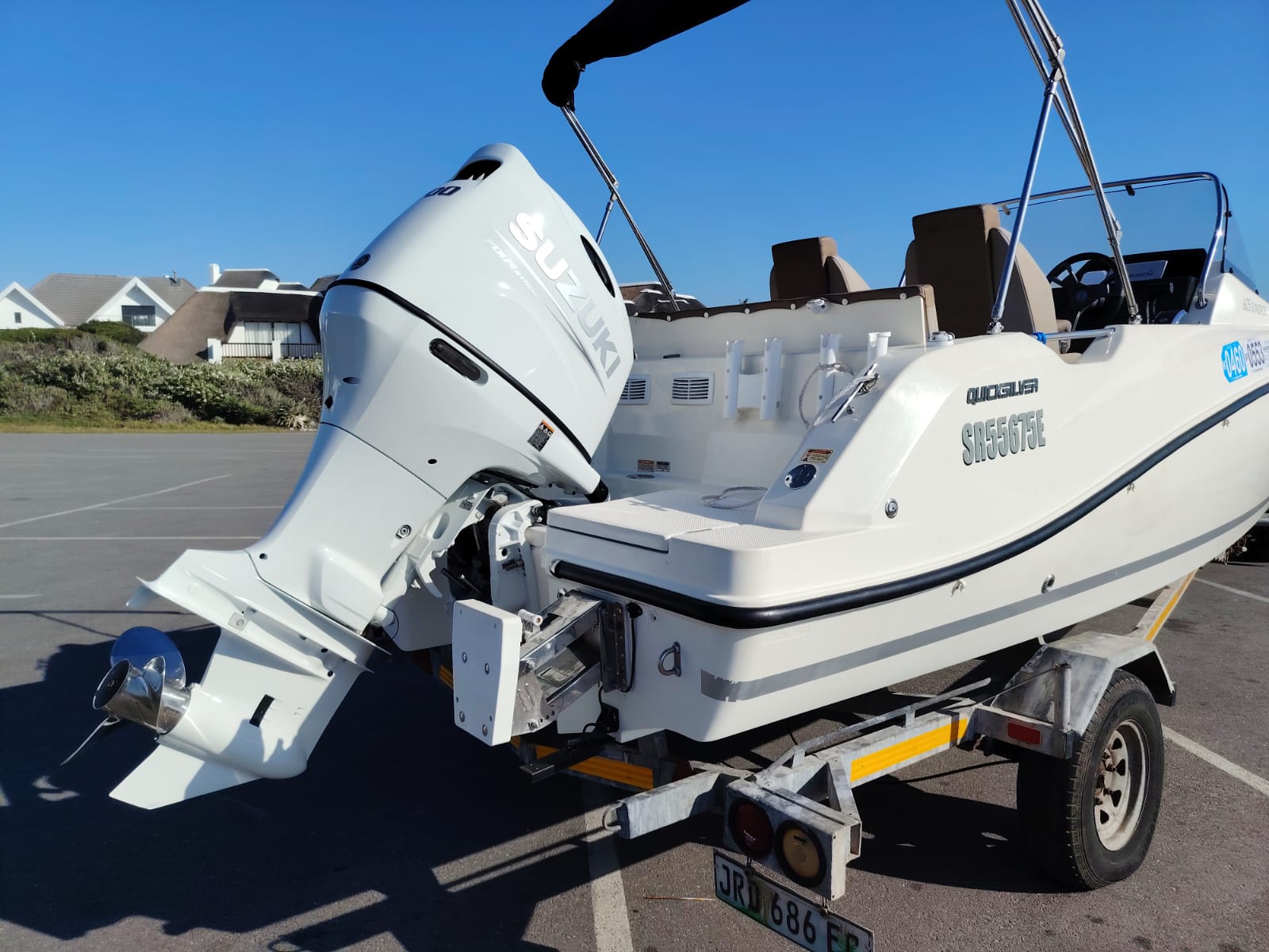 White boat with outboard motor on a trailer in a parking lot.